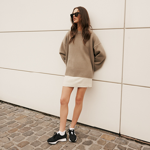 Frau trägt weiße FALKE Cool Kick Sneakersocken vor einer Betonwand