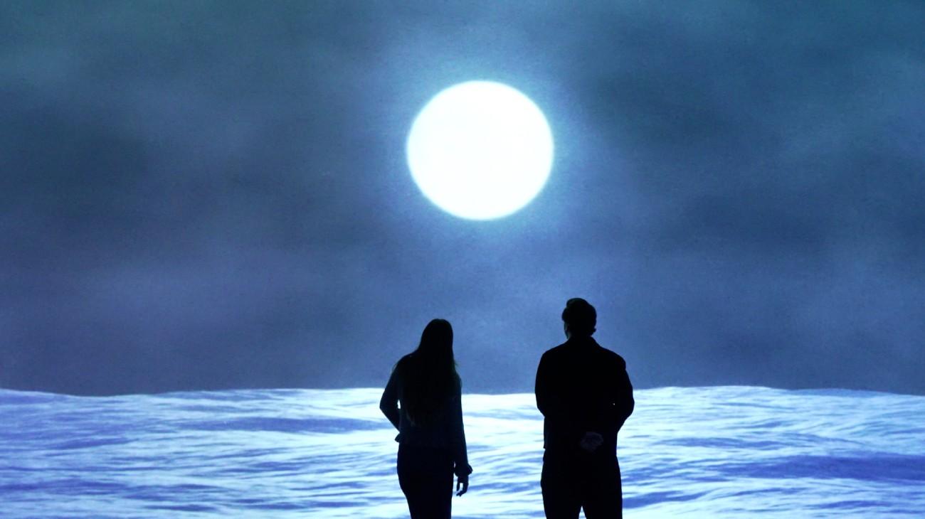 Visitors silhouetted before a moonlit projection inside an immersive Frameless gallery