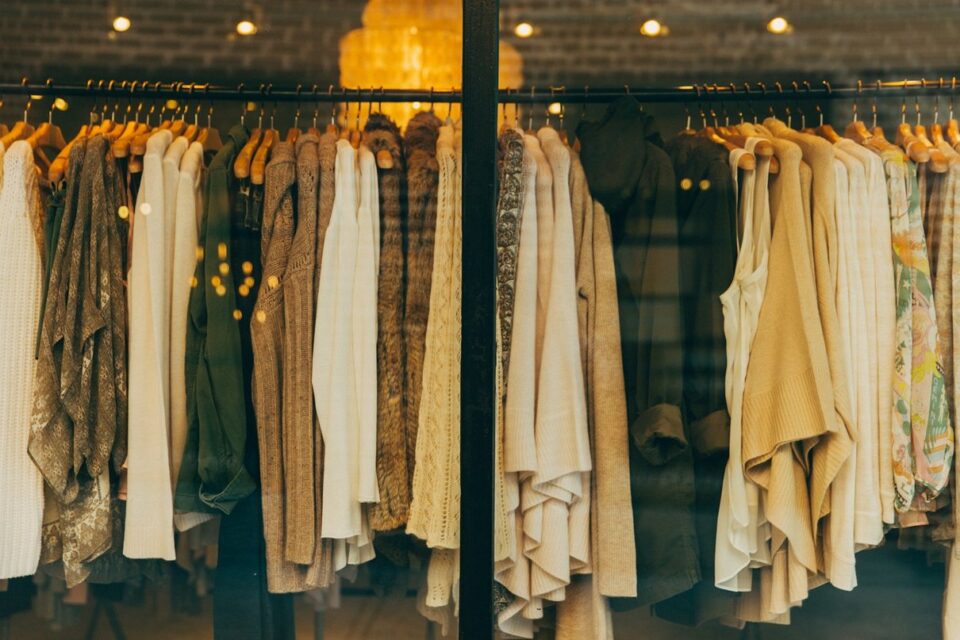 Warmly lit fashion boutique window filled with hanging knitwear and clothing