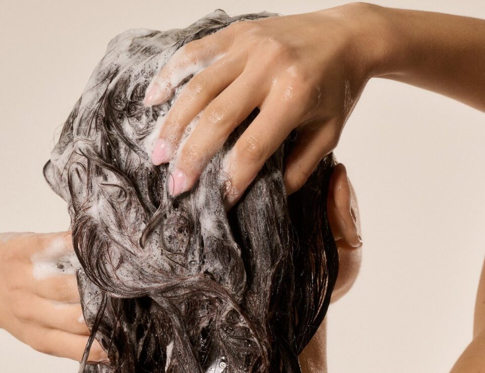 Woman washing her foamy wet hair in a shower