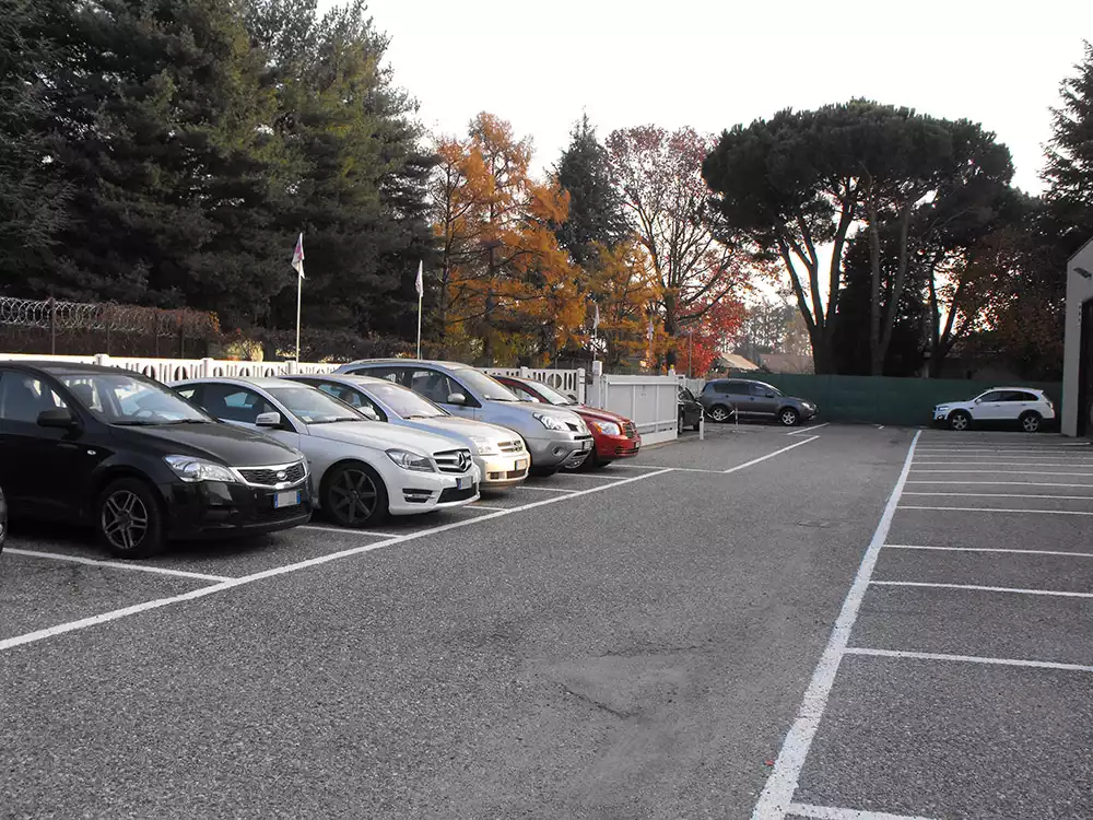 Cars parked in a fenced airport parking area bordered by autumn trees