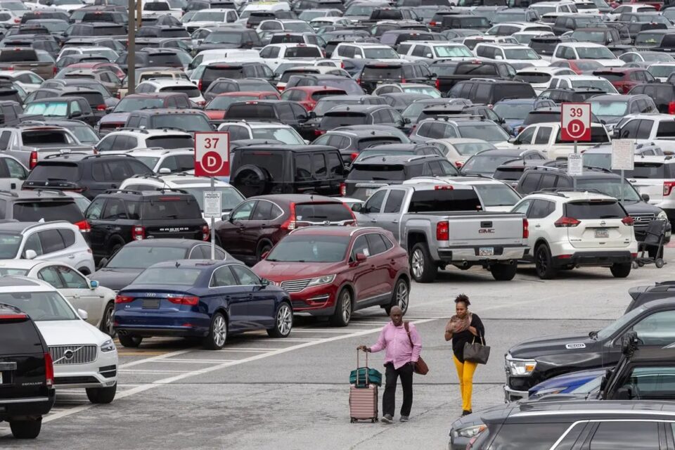 Travellers with luggage walking between parked cars at an airport