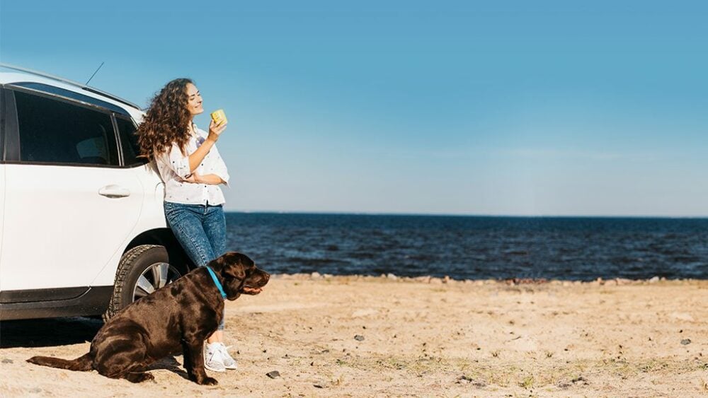 Frau mit Hund neben einem Auto am Strand